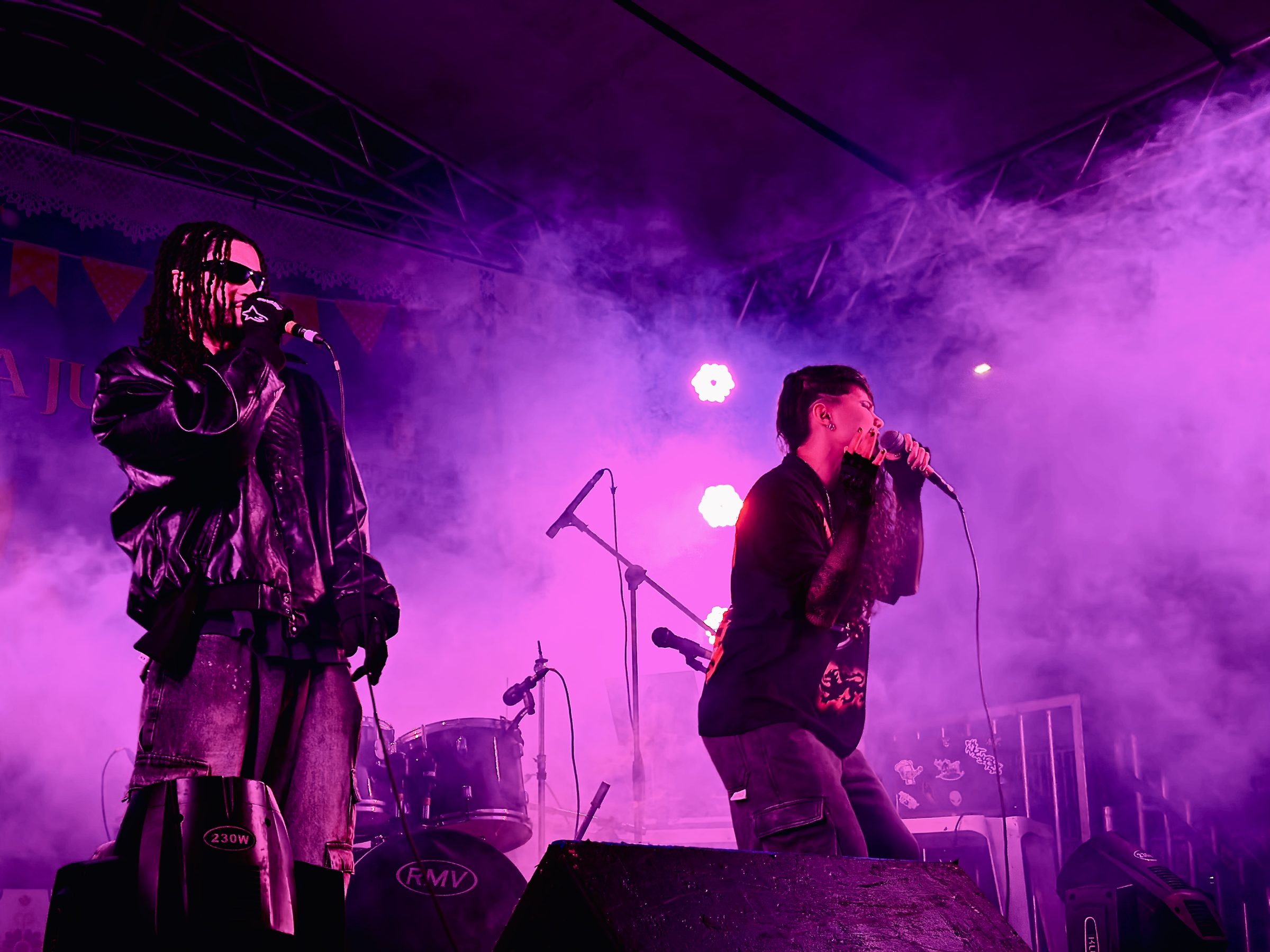 Dois artistas cantando ao vivo sob luz roxa no show BAILON!, 2026